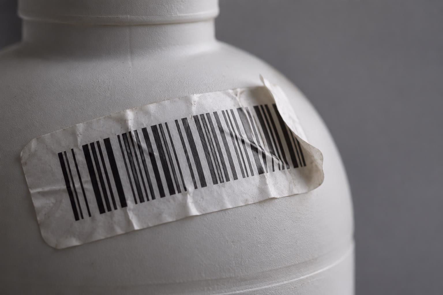 Una etiqueta de código de barras arrugada se despega del hombro curvo de una botella de plástico